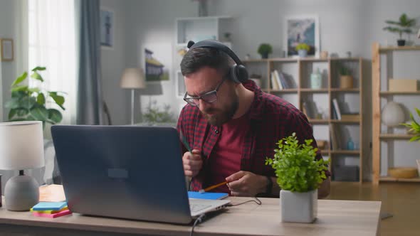 Young Stylish Male in the Red Plaid Shirt and Headphones Listening to Music and Imitating Playing