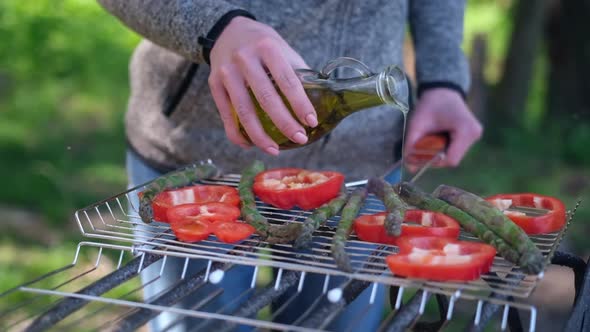 Making Grilled Vegetables  Pouring Olive Oil on Asparagus and Red Pepper on a Charcoal Grill