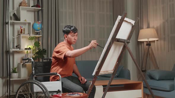 Asian Artist Boy In Wheelchair Holding Paintbrush Mixed Colour And Painting On The Canvas