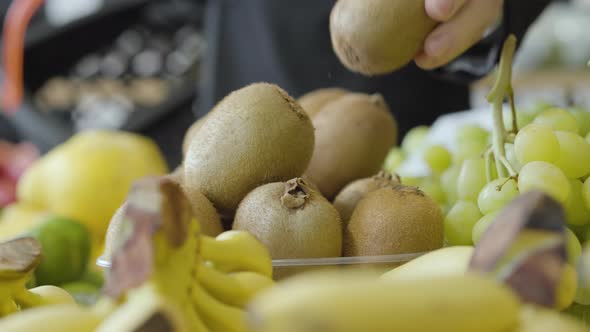 Close-up of Kiwi Fruits Lying on Shelf in Grocery As Unrecognizable Man Putting One Into Shopping