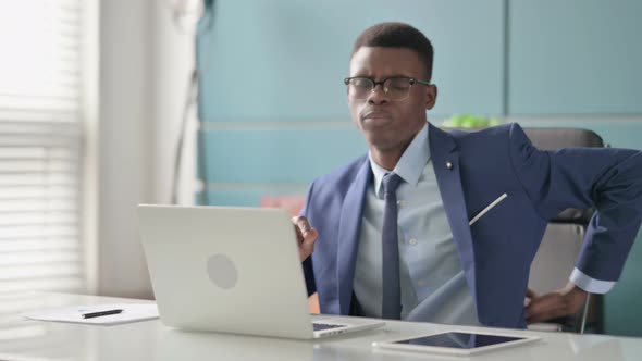 Young African Businessman Having Back Pain While Using Laptop in Office