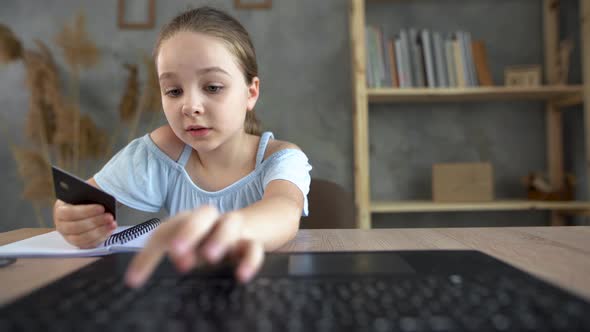 A Young Online Shopper Girl Sits at the Table at Home and Enters a Credit Card Number on a Laptop