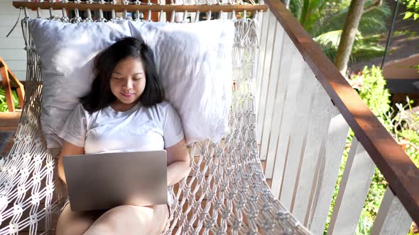 Freelancer Asian woman using laptop online working and sleep on beach hammock