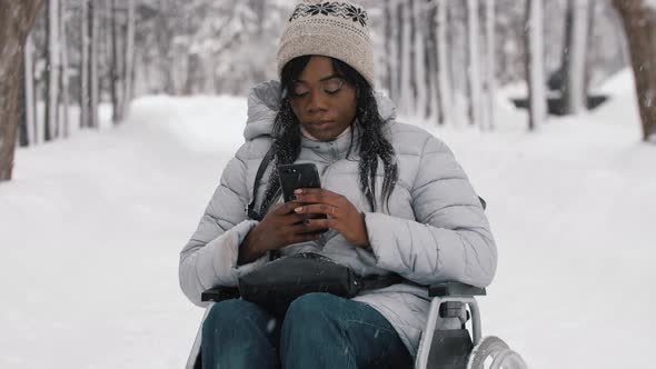 Young Black Woman Sitting in a Wheelchair and Using Her Phone in Winter Forest