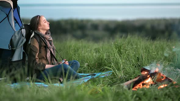 Relaxed Backpacker Female Sitting at Camping Tent Near Campfire