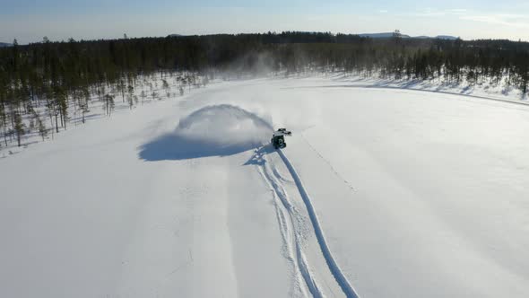 Aerial view above tractor digger blowing snow creating frozen trail in rural Sweden wilderness