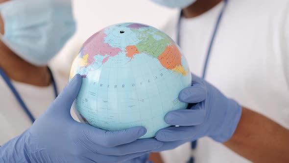 Diverse Couple Of Volunteers Wearing Face Masks Holding Earth Globe