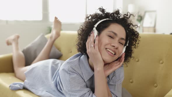 Happy Latina American Woman Relaxing on Sofa Listening to Music