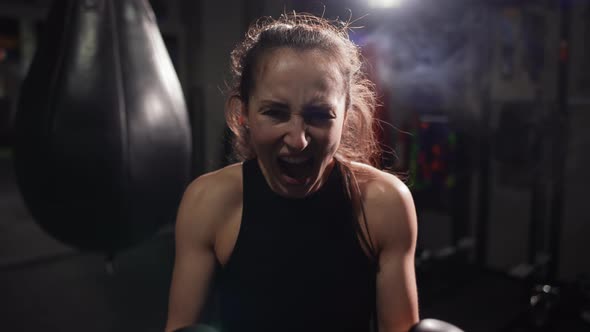 Female Boxer Standing at Dark Gym Looking Intensely at the Camera and Screaming
