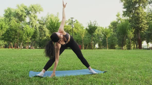 Young Fit Woman Practicing Triangle Pose Yoga in Park at Sunset