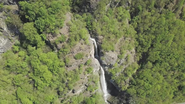 Aerial drone shot over green forest and a tall waterfall over grey mountain rocks in Switzerland.