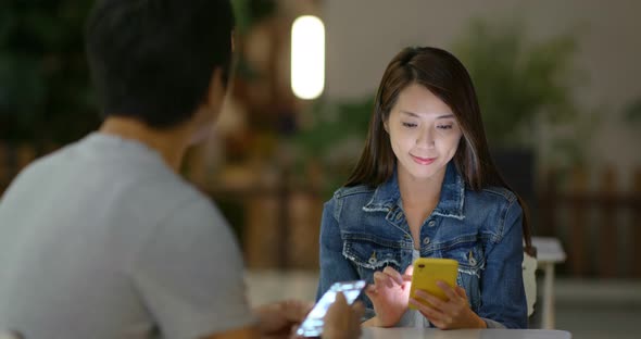 Man and woman use of mobile phone together at night in outdoor coffee shop