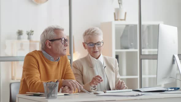 Two Mature Colleagues Working on Presentation Together in Office