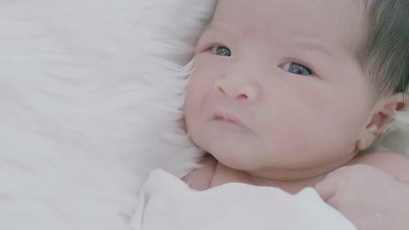 Close up face of Asian new born baby laying on a soft blanket.