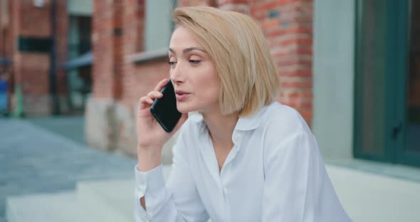 Woman Sitting on Steps, Stairs, Talking on Mobile Phone on Urban Street Background.