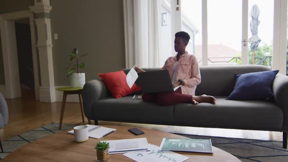 African american woman reading a document and using laptop while working from home