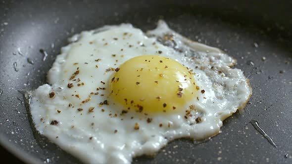 Close up footage of a seasoned egg being baked in a black dry frying pan