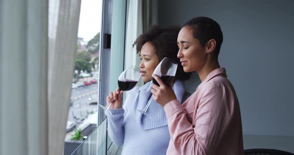 Lesbian couple drinking red wine at window