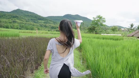 Girl Running With Paper Airplane In Rice Field alt