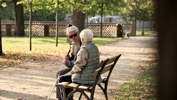 Elderly Caucasian Woman with Her Handicapped Husband in the Park Husband is in Glasses and a Stick