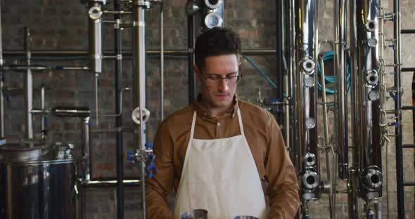 Portrait of happy caucasian man working at gin distillery using equipment and smiling to camera