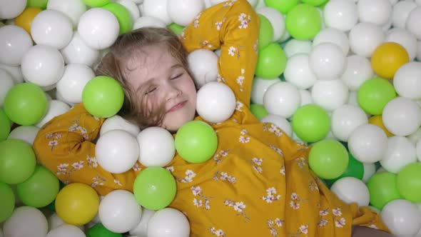 a Little Girl Plays in a Dry Pool with White Yellow and Green Plastic Balls