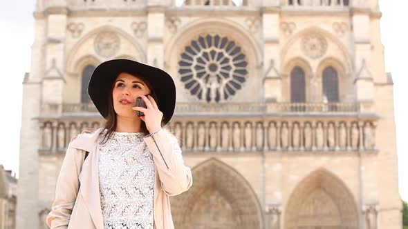 Woman in Paris using her mobile phone with Notre Dame cathedral on background