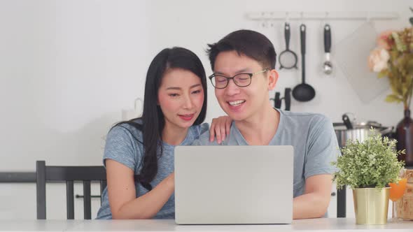 Young Asian couple enjoy shopping online on laptop happy buy ecommerce after have breakfast at home.