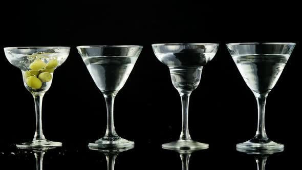 Green olives being dropped into four cocktail glasses