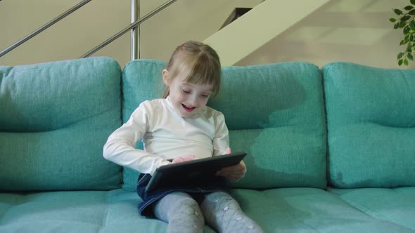 Curious Little Kid Girl Using Digital Pad Entertainment Device Sitting On Sofa Alone.