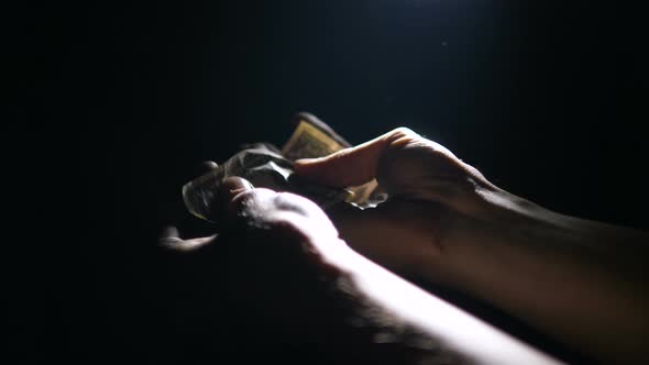 Dollar Bill Falls Into Hands of Man in Dark in Counter Light, Man Unfolds Dollar