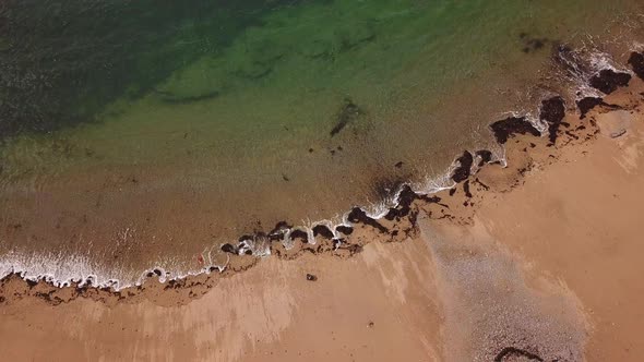 Ascending Birds-Eye Aerial View of Woman Picking Up Trash on Shoreline of a Beach