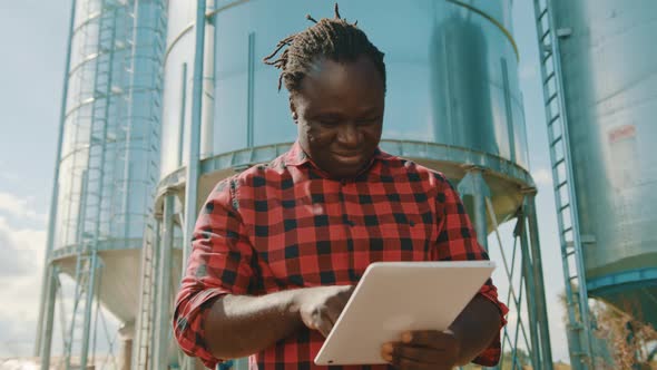 Young Handsome African Man, Engineer Using Tablet in Front of Silo System