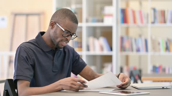 Disappointed Young African Man Doing Paperwork in Library