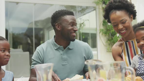 Happy african american family talking and having breakfast in garden