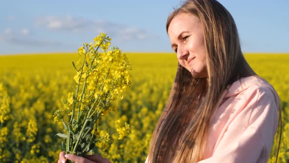 Attractive Blonde of European Appearance Admires a Bouquet of Rapeseed Flowers
