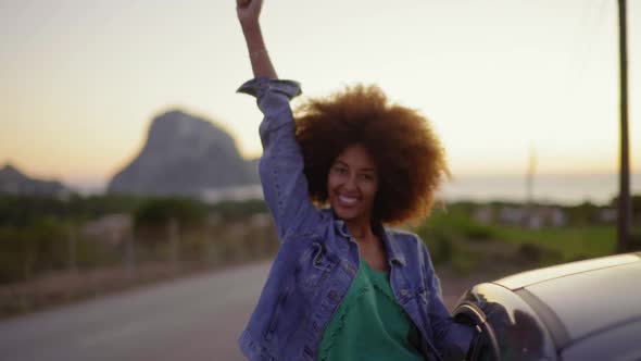 Slow motion shot of young woman during road trip with raised arms