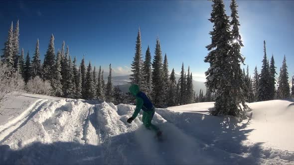 Young female snowboarder riding fresh powder snow in beautiful snowy mountain in sunny winter.