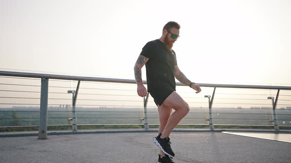 Bearded Man in Sunglasses Warms Up Legs on Footbridge
