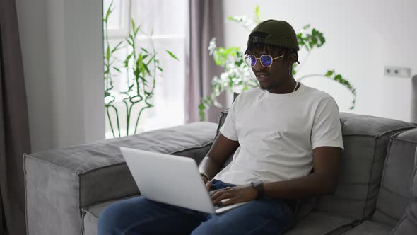 Attractive African American Man in Glasses Sitting on the Sofa Using Laptop at Home