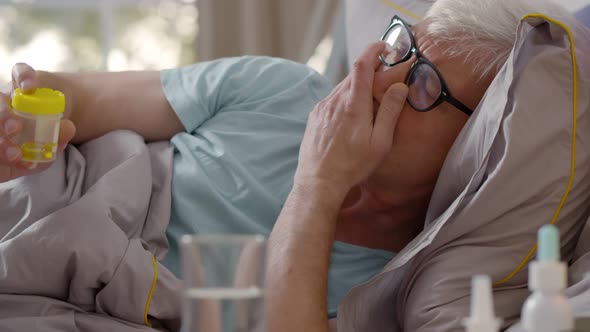 Portrait of Retired Sick Man Taking Heartache Pills Lying in Bed at Home