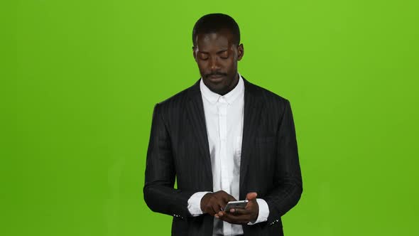 African Is Holding a Phone and Flipping Through Information. Green Screen