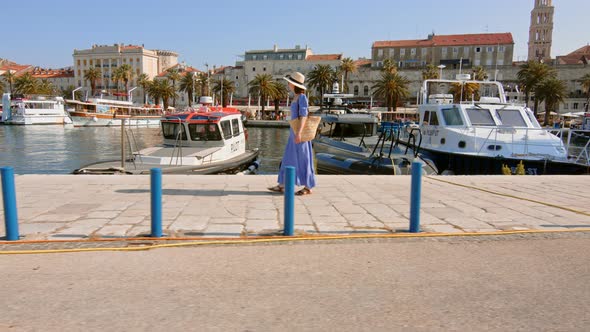 A young girl in a blue dress walking along the pier in the city. Split, Croatia