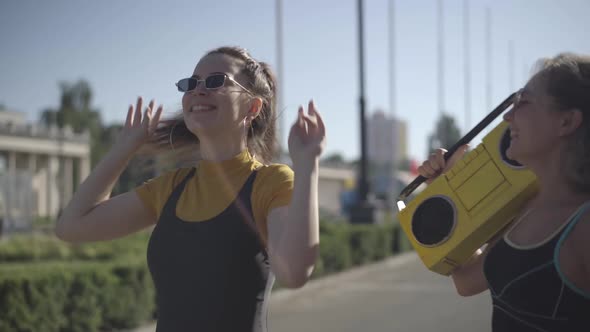 Two Positive 1980s Women in Sunglasses Dancing To Retro Disco Music From Vintage Yellow Tape