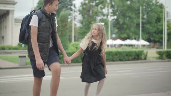 Pretty Girl Walking To School Holding Brother's Hand. Portrait of Little Cute Caucasian Schoolgirl