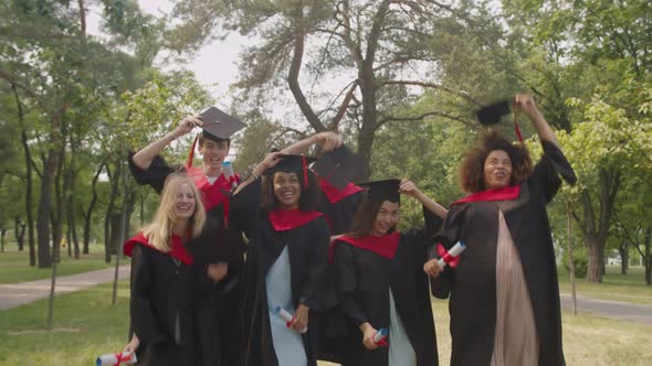 Cheerful Diverse Multiracial Graduates Celebrating Graduation Day Tossing Up Mortarboards in the Air