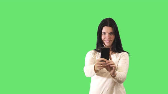 Smiling Black-haired Caucasian Woman Taking Photos with Smartphone at Green Background. Portrait of