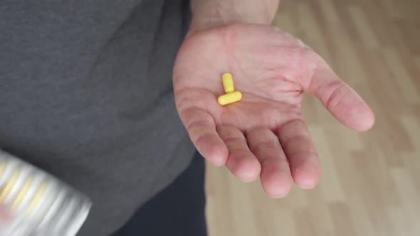 Close Up View of Male Hand Holding Yellow Capsules