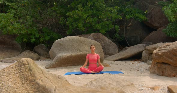 Front Shot of Sport Woman She is Meditating By Sitting on the Beach Against the Jungle Forest