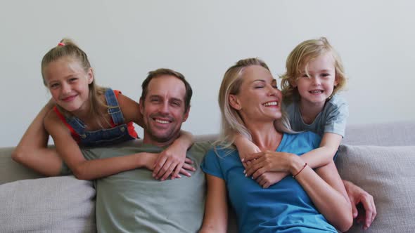 Portrait of smiling caucasian parents on sofa with son and daughter embracing them